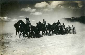 "A horse drawn United States Army artillery battery crosses an open, dusty area"