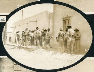 Maderista soldiers stand along a sidewalk by adobe buildings