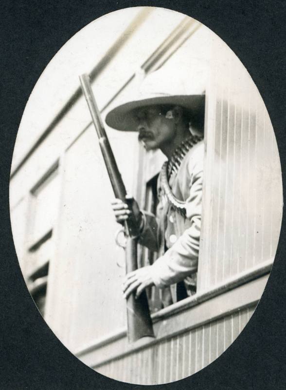 Armed soldier leans out of a window of a railroad car and keeps watch.