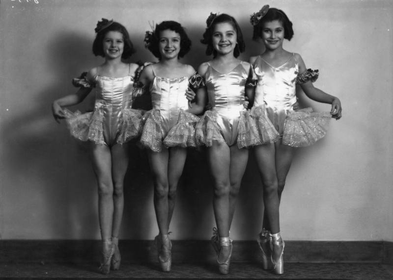 Four girls stand en pointe in ballet costumes