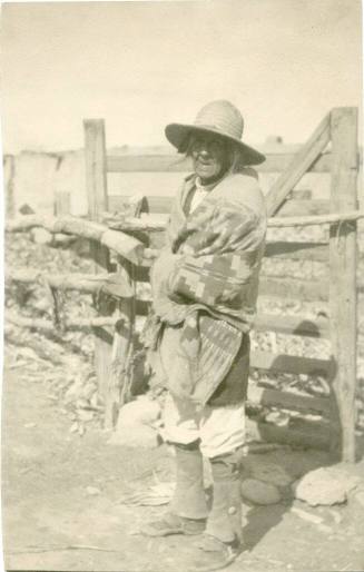 Elderly Native American man standing next to a fence wrapped in a blanket