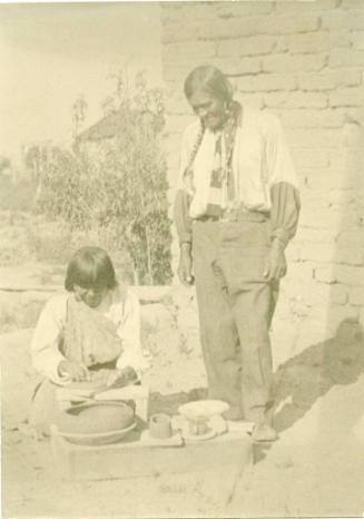 San Ildefonso man watches as a woman makes a pot
