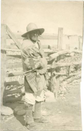 Elderly Native American man standing in front of fence wrapped in blanket