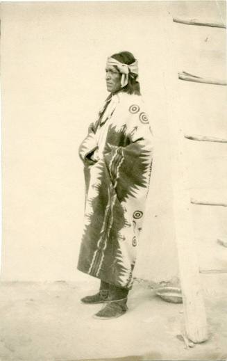 Native American man wrapped in blanket stands next to a ladder
