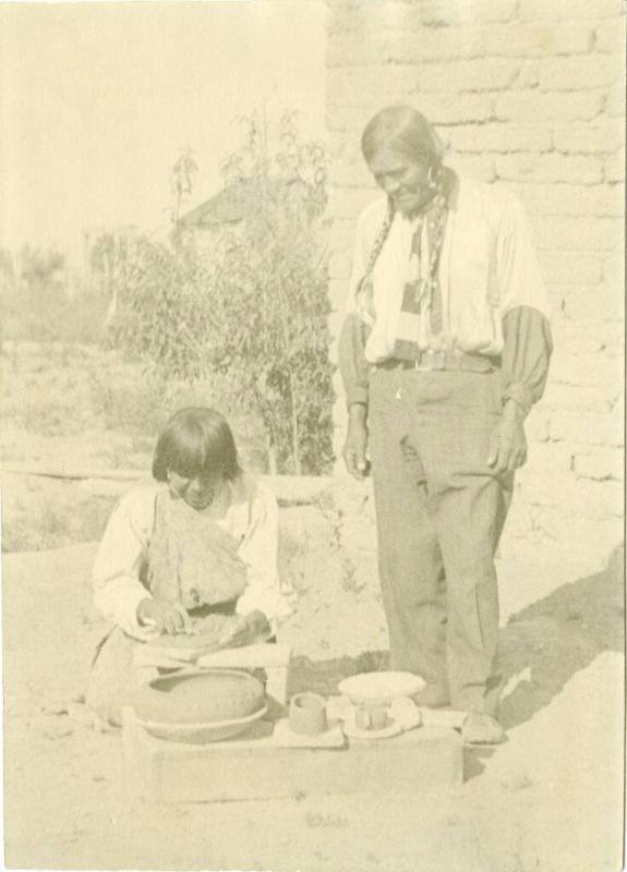 San Ildefonso man stands, watching a woman make a pot