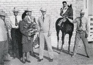 A group of people stand with a large trophy and a race horse