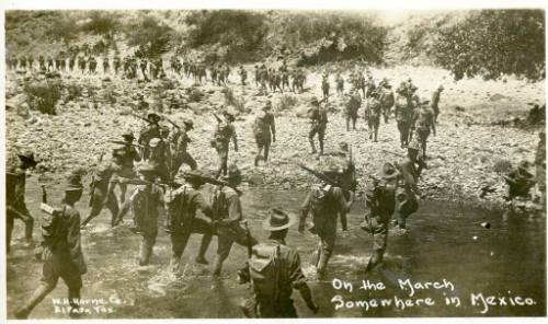 American soldiers wade a stream and march up the shore