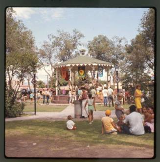 People sit on the grass and stand around the gazebo in Old Town