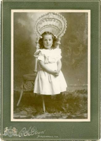 Portrait of an unidentified young girl standing in front of a tall chair