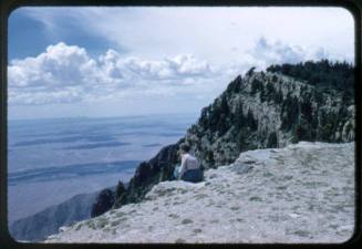 A woman sits on the edge of the crest of the Sandia Mountains