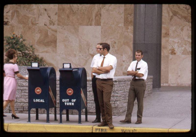 Three men stand next to mail boxes outside the United States Post Office