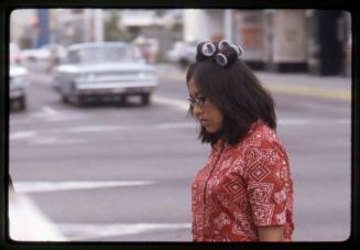 A woman with curlers in her hair crosses a street