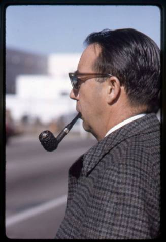 A man with a pipe in his mouth waits to cross a street