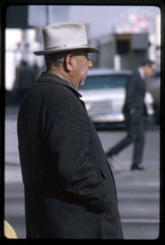 A man in a black coat waits to cross a street