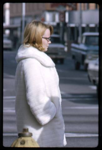 A woman in a white coat waits to cross a street