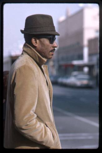A man in a brown coat waits to cross a street