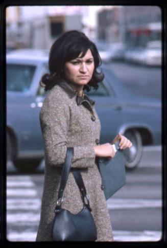 A woman in a brown coat waits to cross a street