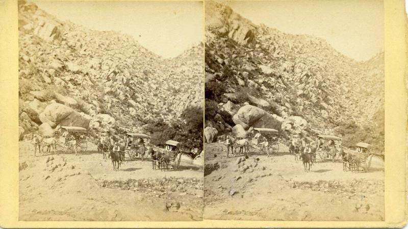 Horse drawn wagons at the base of a rocky hill
