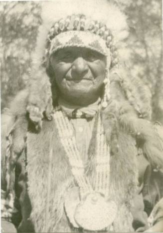 Native American man wearing headdress and large necklace and animal hides
