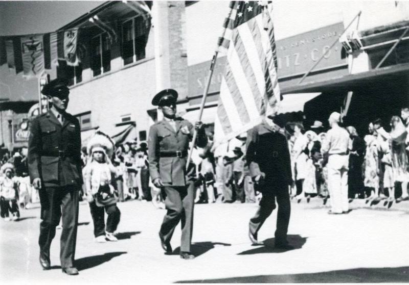 Three men in military dress lead children in a parade