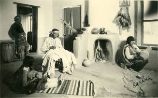 Four Native Americans in a room of a house, with a fireplace and a cat