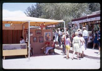 Artists sit in vendor booths at an arts & crafts fair