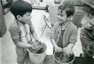 Two boys play with buckets of mud