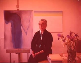 Georgia O'Keeffe sitting by easel painting